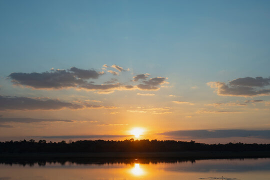 Sunset sky over calm lake with cloud reflection and dark tree line, warm golden evening light
