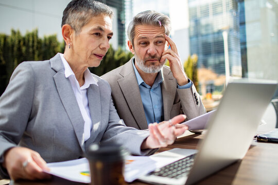 Two senior business colleagues reviewing data on a laptop in the city