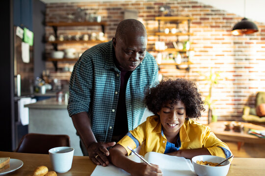 Older man helping child with homework in kitchen