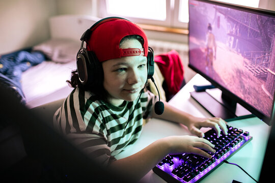 Teen gamer with headset playing pc in bedroom