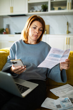 Worried woman checking bills on phone at home