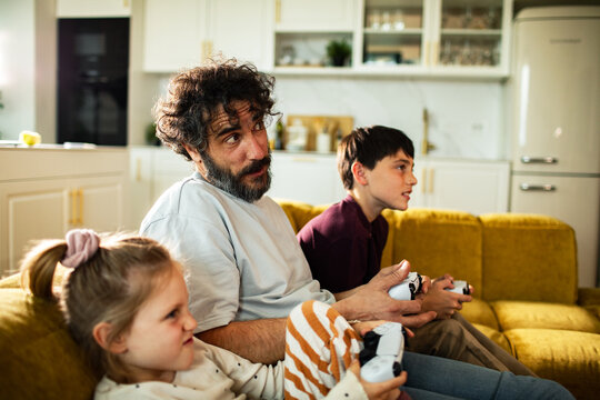 Father and kids playing video games on sofa at home