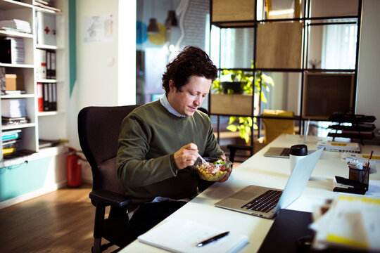 Man eating salad at work desk in modern office