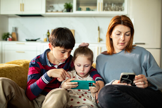 Mother and children using smartphones on sofa at home
