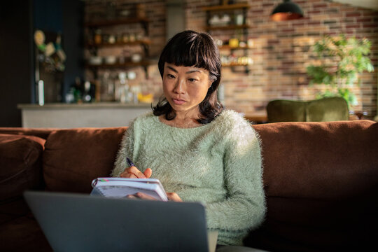 Woman taking notes on couch while working from home