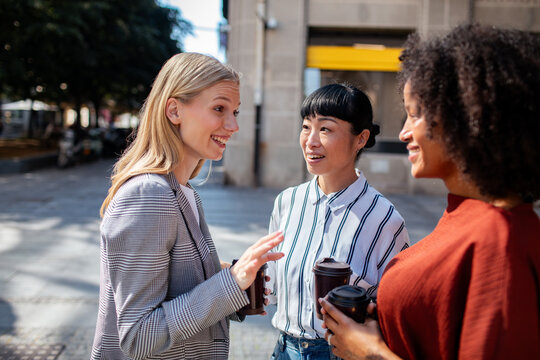 Three colleagues chatting with coffee on city street