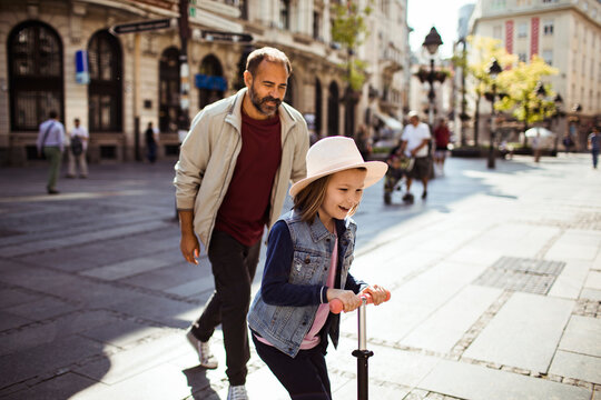 Father and daughter riding scooter on city pedestrian street