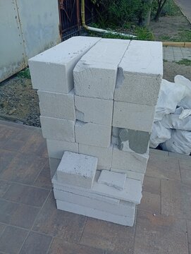 A stack of lightweight aerated concrete blocks on a paved ground at a construction site, grey porous building material bricks for wall masonry and house renovation outdoor.