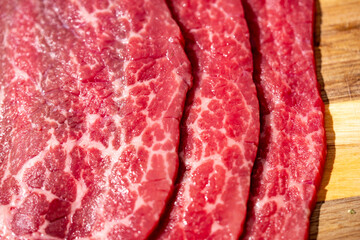 Obraz premium Raw beef steaks with natural fat marbling. Raw beef slices prepared for cooking. Close-up raw beef texture with intramuscular fat. Fresh raw beef on wooden cutting board.