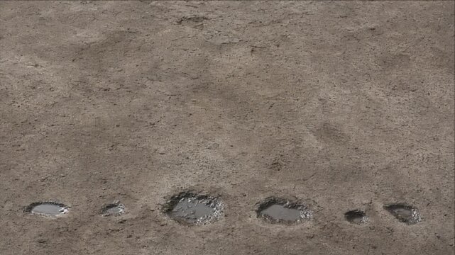 Minimal cinematic timelapse background of puddle beside soil trail across rough gray earth, combining wet footprints, muddy ground, quiet natural texture, abstract pattern, and atmospheric travel