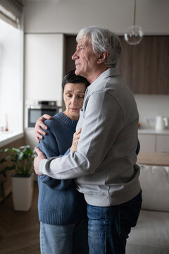 Tired mature wife with closed eyes being tightly embraced by husband, seeking comfort and emotional support. Loving couple facing emotional distress, exhaustion, family crisis and life challenges. 