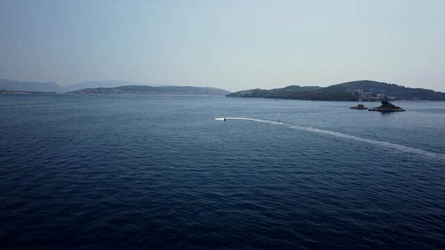 Motorboat crosses Adriatic Sea near Seget Vranjica, Trogir, Croatia and islands, aerial dolly tracking follows jetski racing across surface, abstract entertainment