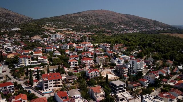 Seget Vranjica, Trogir, Croatia red roof homes spread across a coastal hillside, aerial ascend tilting down across churches and orange homes