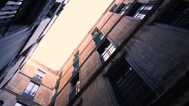 Historic Barcelona courtyard walls rise toward bright sky with rows of windows and balconies, orbit upward angle
