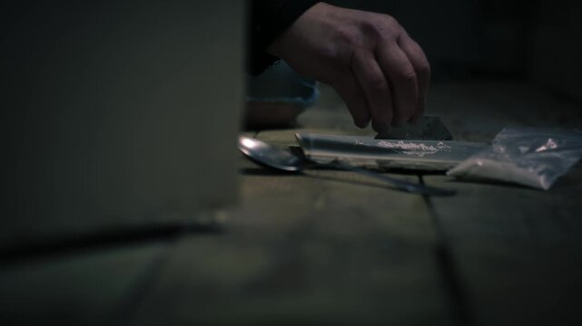 Addict cutting illegal drugs in dark room through view of opening door close up 4k shot shot slow motion selective focus