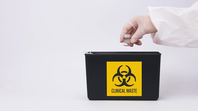 Cautious person performs medical waste disposal dropping sharp syringe into yellow biohazard safety container with protective glove hand in clinic