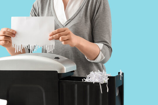 Data privacy and document security, woman shredding confidential paper with a paper shredder on a blue background