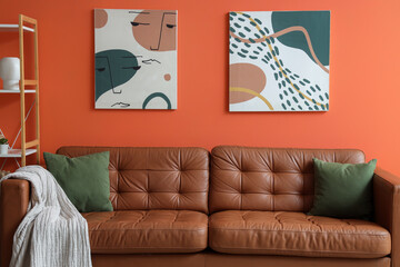 Modern living room interior design with brown leather sofa, green pillows, and abstract art on a vibrant orange wall © Pixel-Shot
