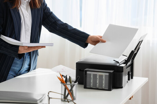 Businesswoman with paper sheets using printer on desk in office