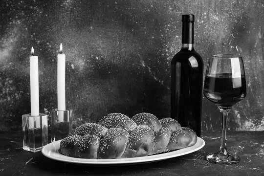 Traditional challah bread with wine and burning candles on grey grunge table. Shabbat Shalom