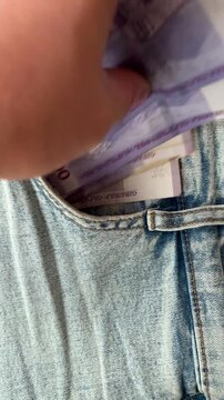 Vertical 4K video. Top view. Male hand pulls of stack of 1000 dram into pocket of blue denim jeans pants. Armenian cash money. Concept of currency exchange, salary, pay tax, debt, loan, bribe, travel