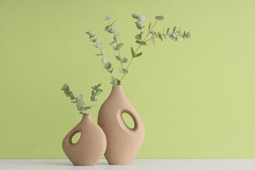 Vases with eucalyptus branches on white table against green wall © Pixel-Shot