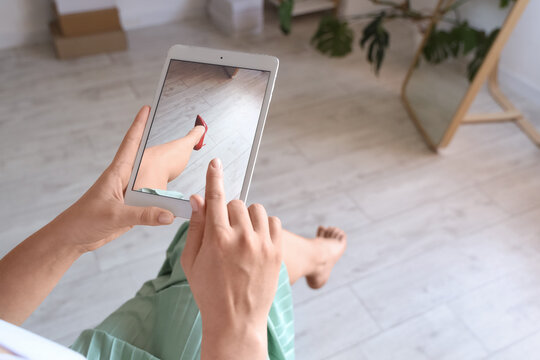 Young woman trying on new shoes with tablet computer at home