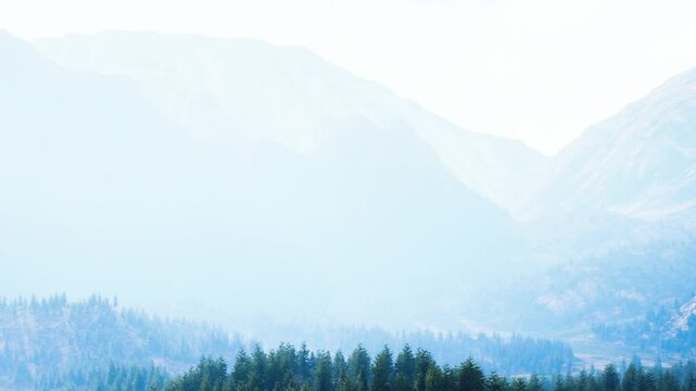 A foggy morning covers high mountains in a remote location. Trees line the foothills while the peaks are barely visible. The scene presents a quiet atmosphere in nature.