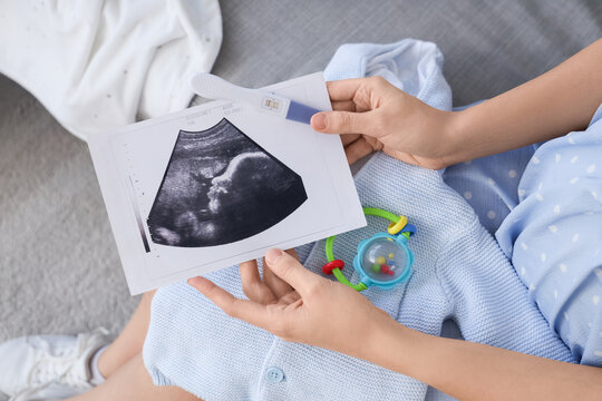 Pregnant woman with sonogram image and pregnancy test on sofa in room. Closeup