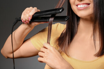 Obraz premium Beautiful young woman straightening hair on grey background, closeup