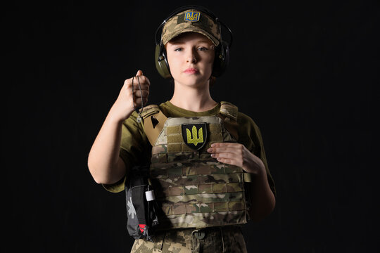 Young female soldier with Ukrainian trident pendant on dark background