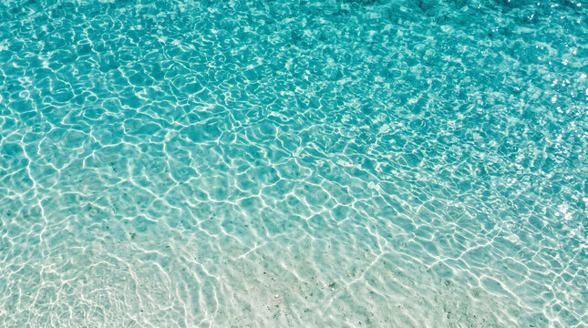 Crystal clear turquoise tropical ocean water surface with gentle ripples and sandy bottom, beautiful natural background for summer vacation and travel concept