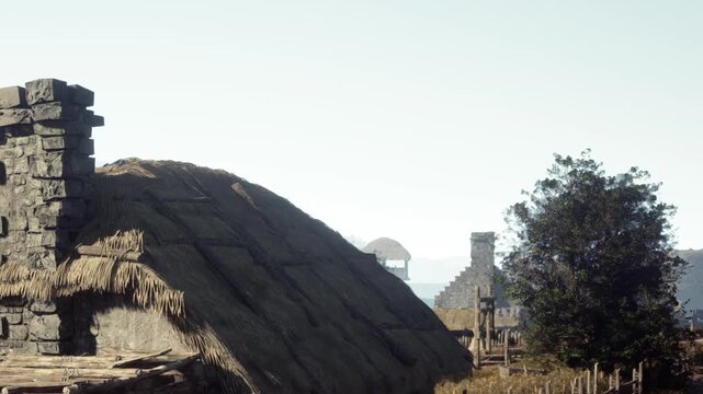 Traditional houses in a rural area. The houses are made of stone and have thatched roofs. Trees surround the area under a clear sky.