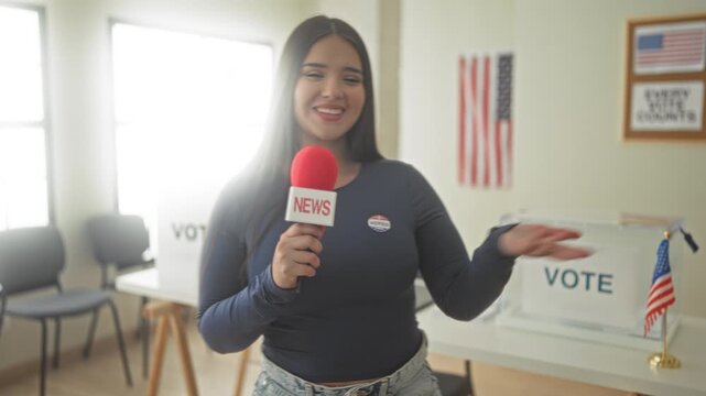 Woman holds red news microphone and points hand to transparent ballot box while wearing voted sticker in voting building; civic pride.