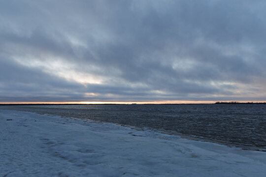Cold evening landscape of northern european waterway covered in slush ice under moody cloudy sky at twilight.