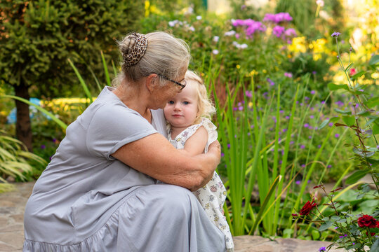 Grandmother Holding Young Granddaughter Close In Flower Garden