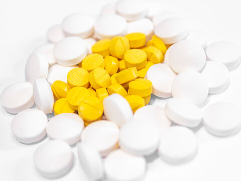 Group of white and yellow medical pills and tablets heap, colorful pharmaceutical background.