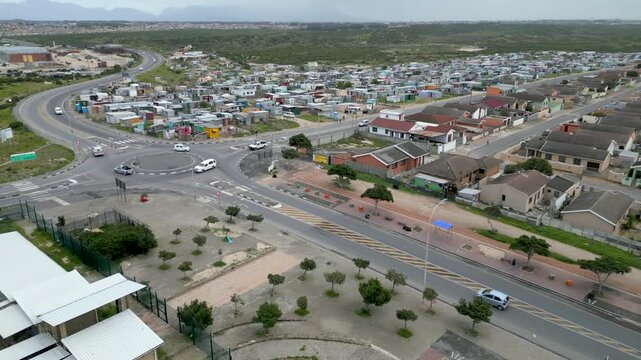 Cars move through a roundabout on the edge of Langa township, dividing informal shacks from formal housing under overcast daylight.