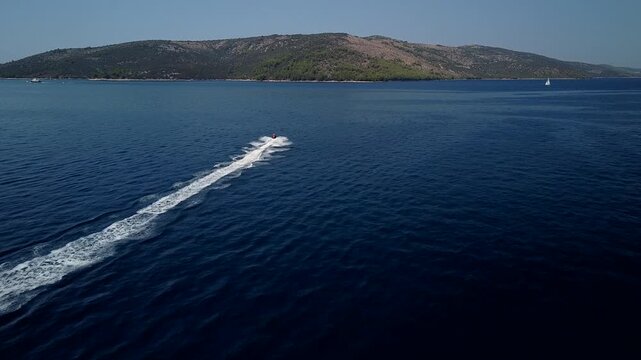 Speedboat crosses blue Adriatic Sea near Seget Vranjica, Trogir, Croatia, aerial rearview tracking follow