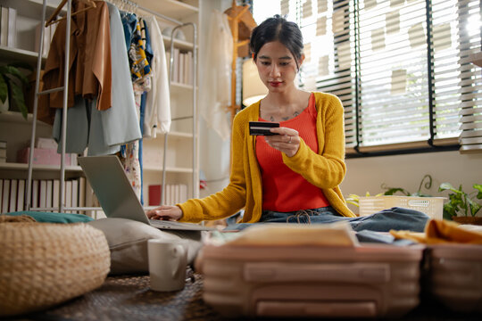 Asian woman using credit card for online hotel booking platform on laptop, representing creative professional women travel payment transaction, e-commerce shopping and holiday planning