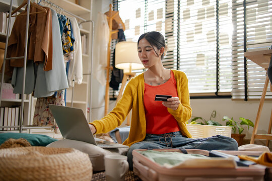 Asian woman using credit card for online hotel booking platform on laptop, representing creative professional women travel payment transaction, e-commerce shopping and holiday planning