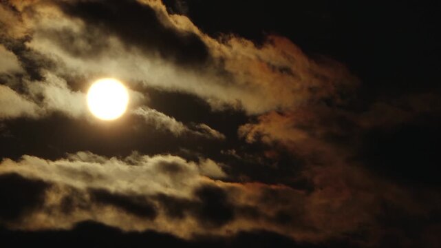 Partial solar eclipse glows in a dark sky as the Moon obscures part of the Sun, while dramatic clouds form a silhouetted layer below.