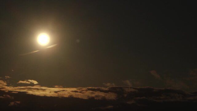Partial solar eclipse glows in a dark sky as the Moon obscures part of the Sun, while dramatic clouds form a silhouetted layer below.