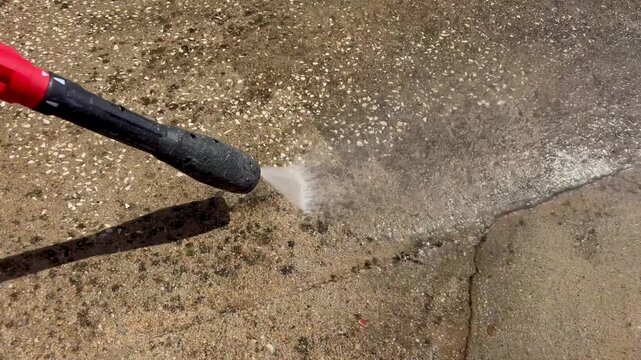 Close up shot of a pressure washer nozzle cleaning a stained concrete floor, removing dirt and marks with a powerful jet of water.