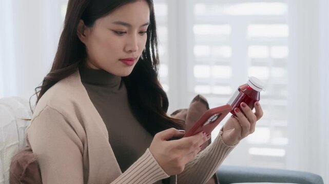 Female Asian holding medicine bottle reading smartphone for health information