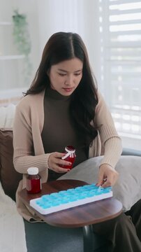 Asian woman organizing pills in a pill box for preparing daily routine medication
