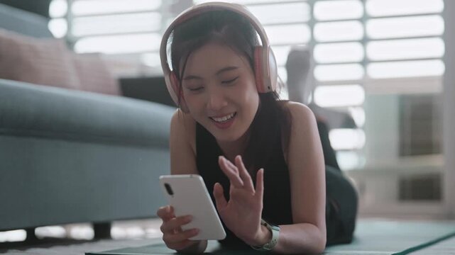 Asian woman in sports attire using phone and headphones indoors