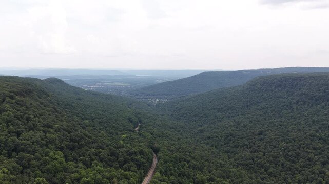 Aerial of winding road through dense forest valley in Marion County Tennessee with curving dirt track cutting through lush temperate deciduous woods and extending over a wide distant valley
