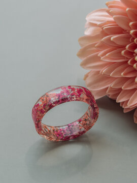 Handcrafted floral epoxy resin ring standing beside pink flower, elegant jewelry composition.