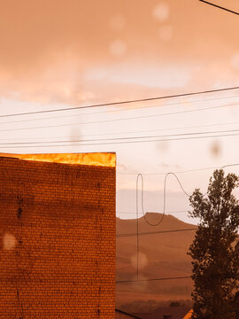 Raindrops on window overlooking industrial landscape in warm orange sunset light.